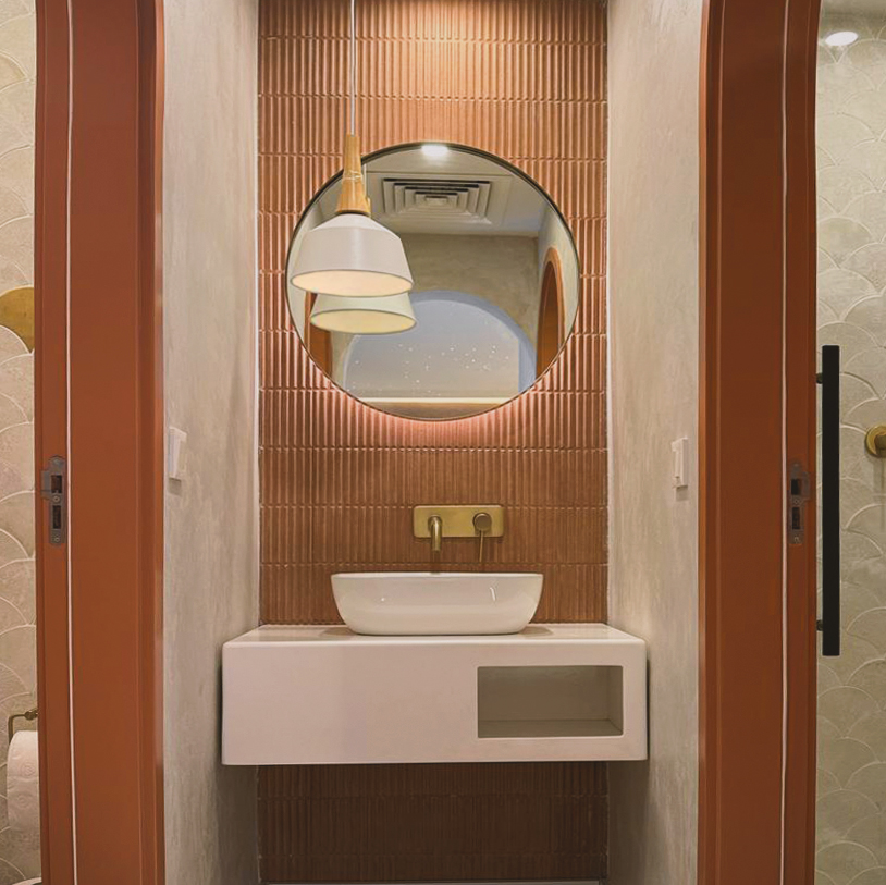 Bathroom at Lumea Pilates with an arched mirror, ribbed terracotta tiling and a stone basin