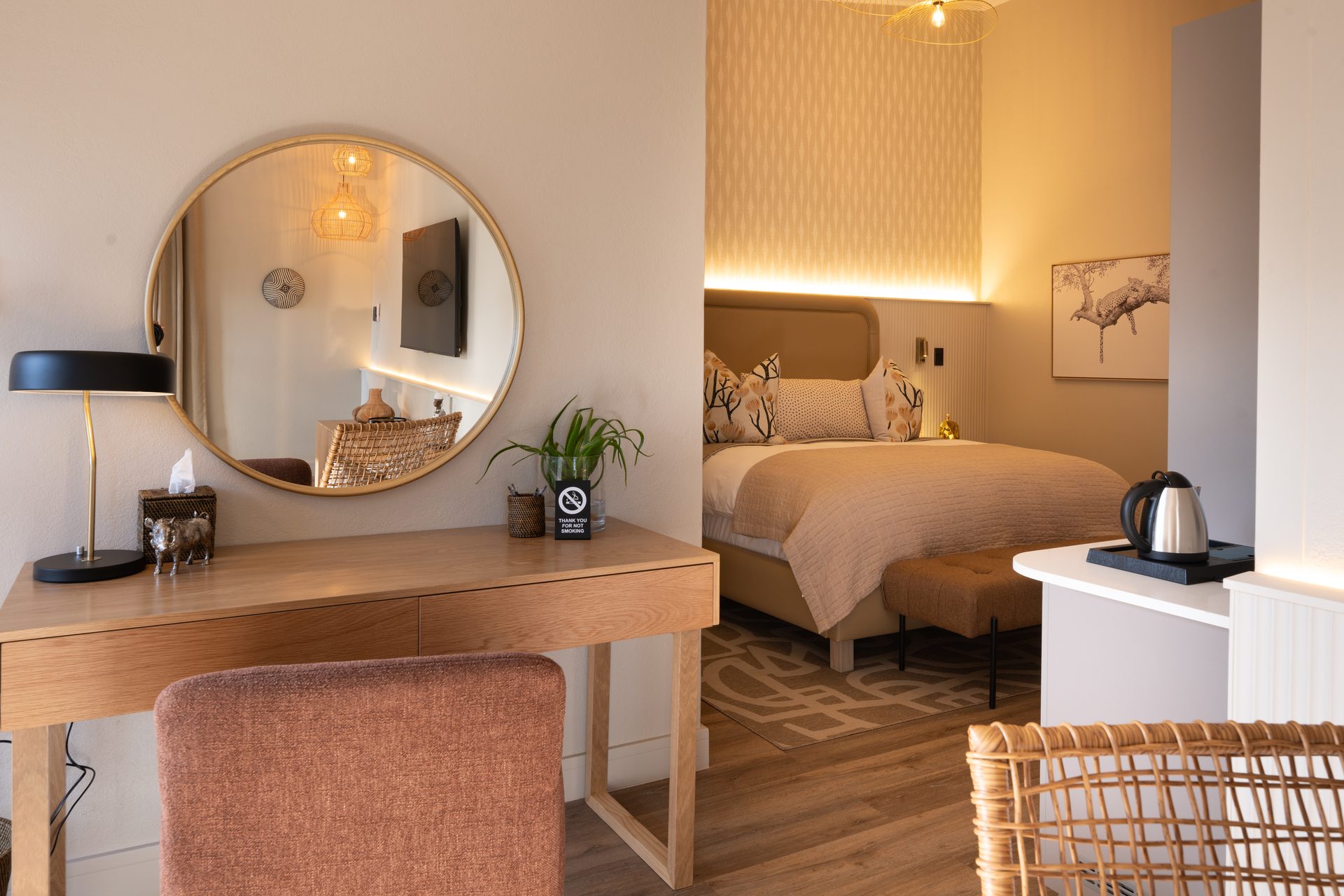 Guest room desk and round mirror at The Ark, with a brass task lamp and woven chair