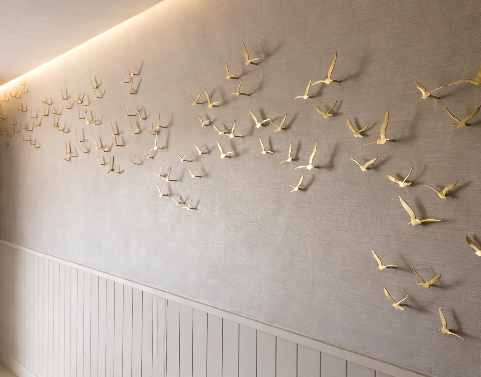 Brass bird flock installation across a plaster wall above ribbed panelling at The Ark