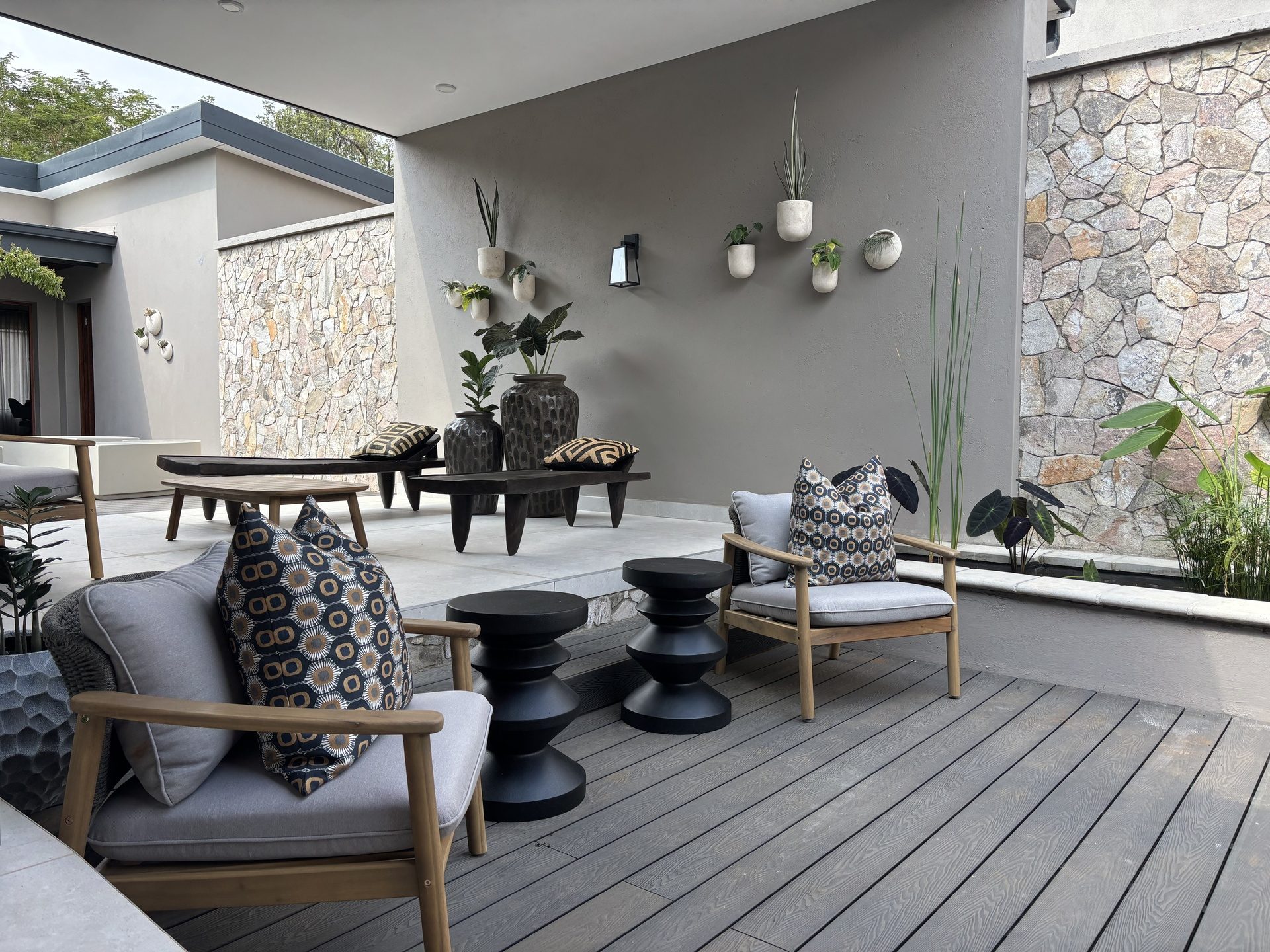 Outdoor lounge at The Ark with patterned cushions, a stone wall and hanging planters